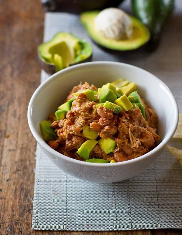 Mexican chicken and pinto beans in a white bowl with avocado. 