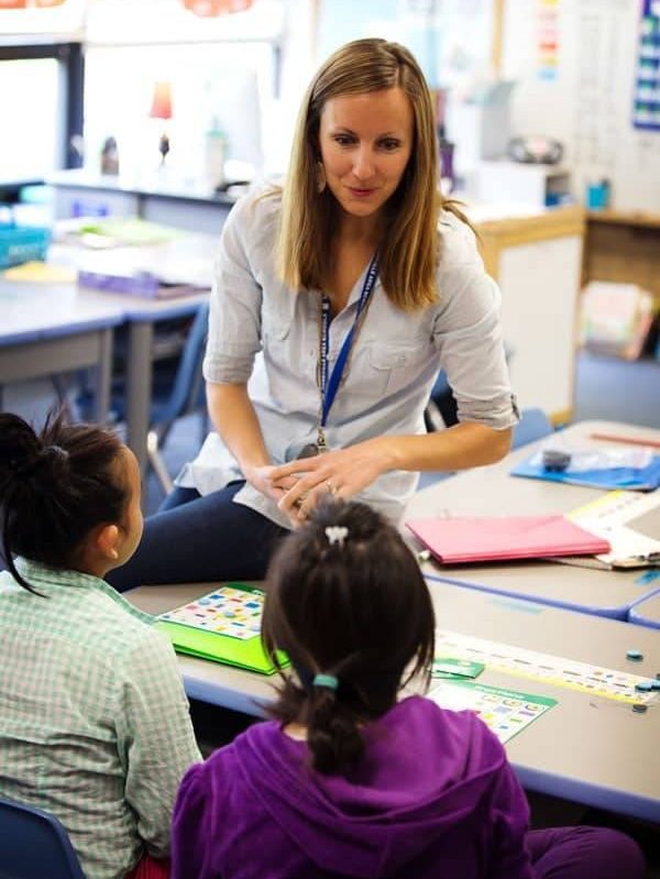 A teacher in the classroom talking to two students.