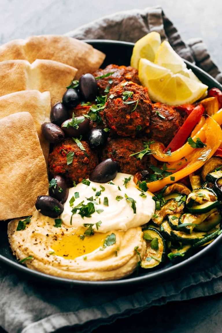 Harissa meatballs in a bowl with hummus, peppers, zucchini, and pita.