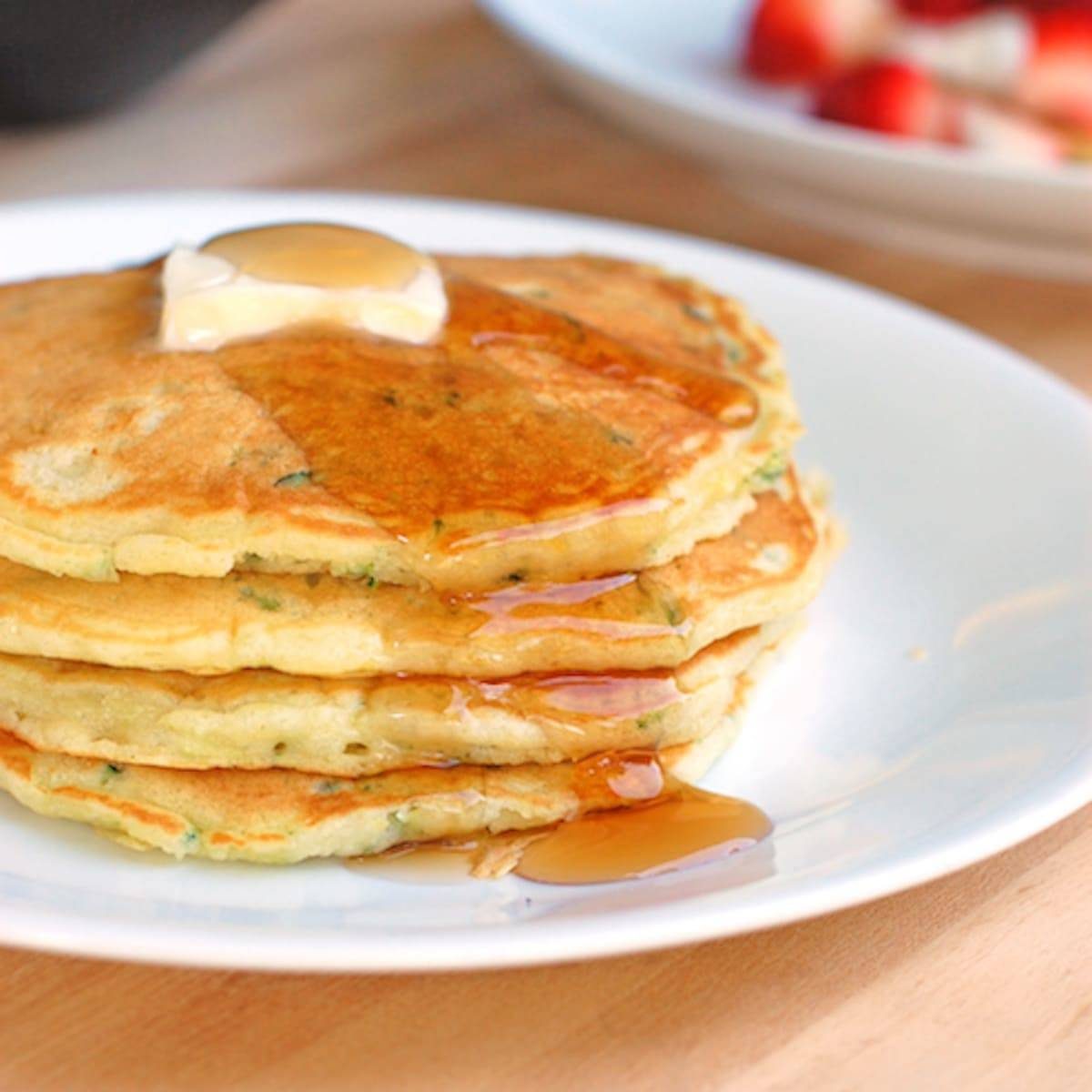 Stack of zucchini pancakes with butter and maple syrup.