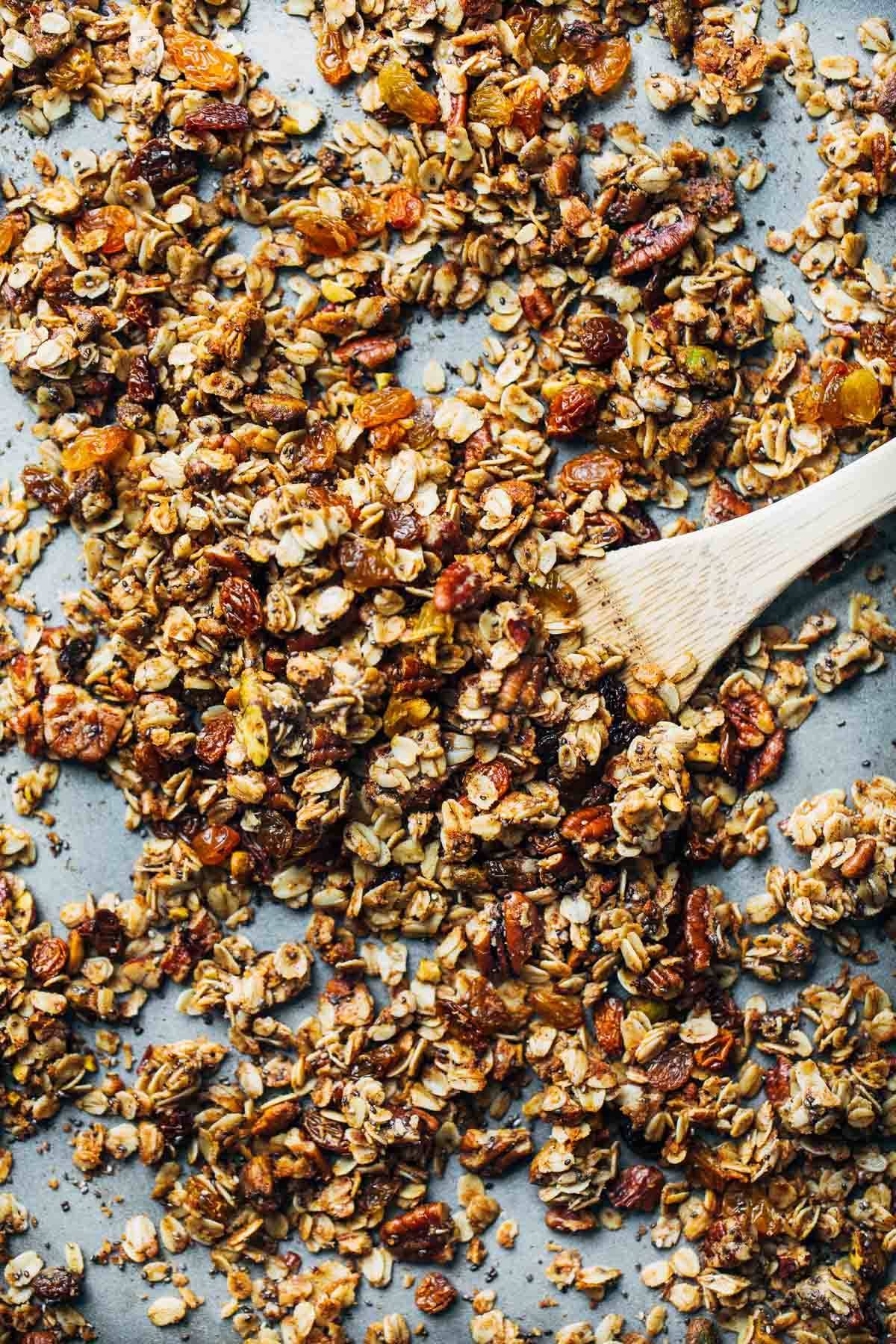 Coconut Oil Granola on a sheet pan with a wooden spoon.